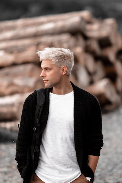a man with white hair standing in front of a pile of logs